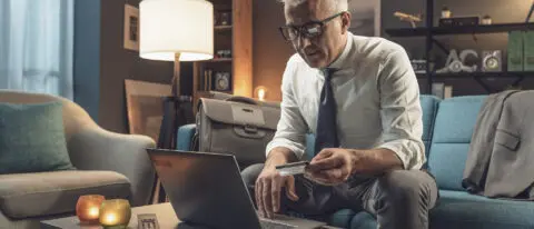 Confident businessman sitting on the couch at home and using his credit card online, he is doing online-banking